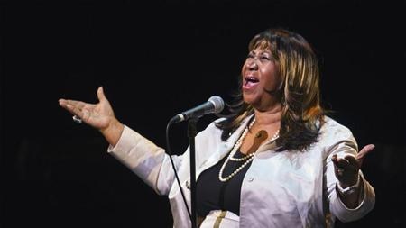 Aretha Franklin with her arms out singing into a microphone on stage