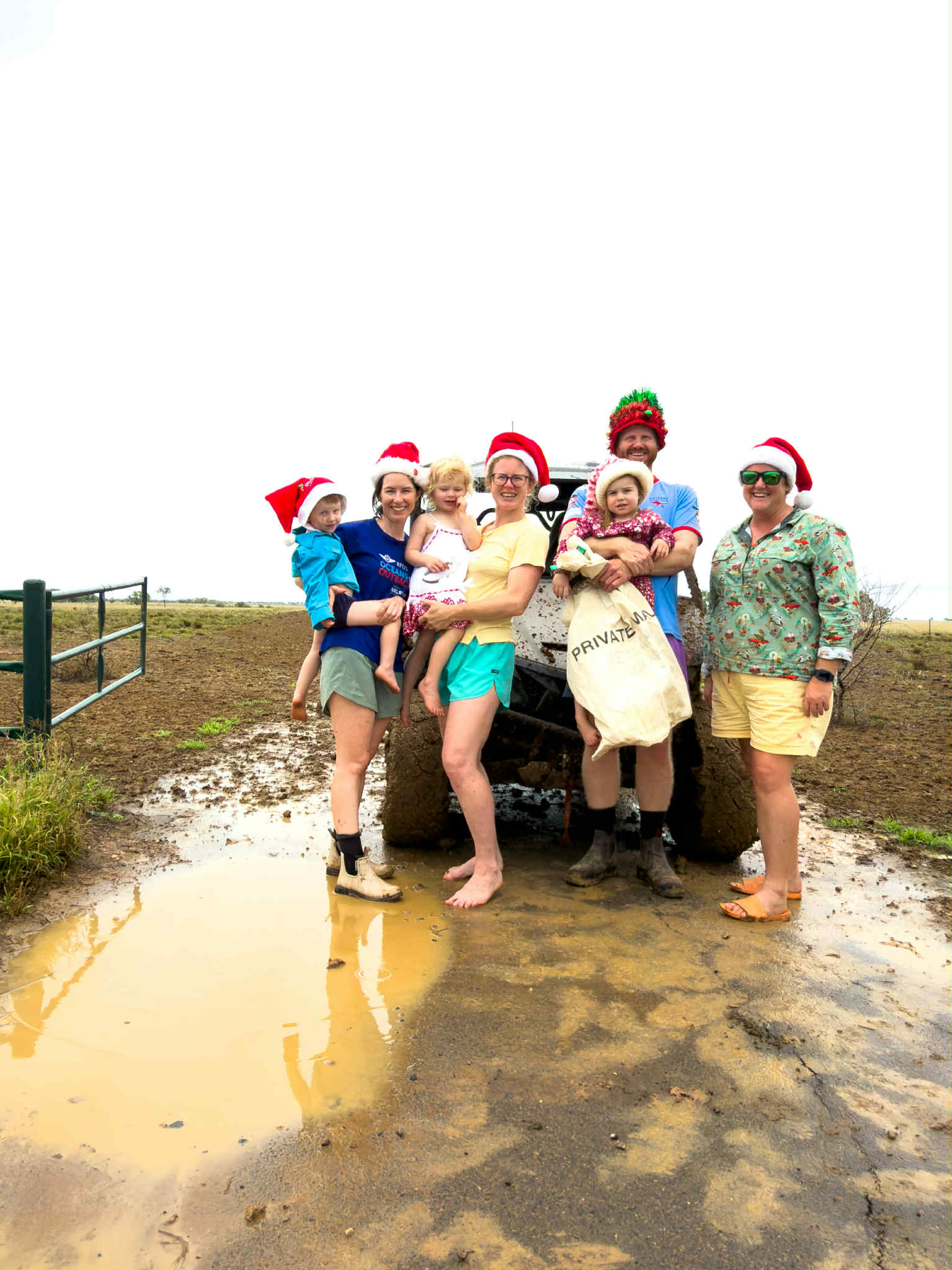 Um grupo de pessoas vestidas com chapéus de Natal em uma cena rural enlameada