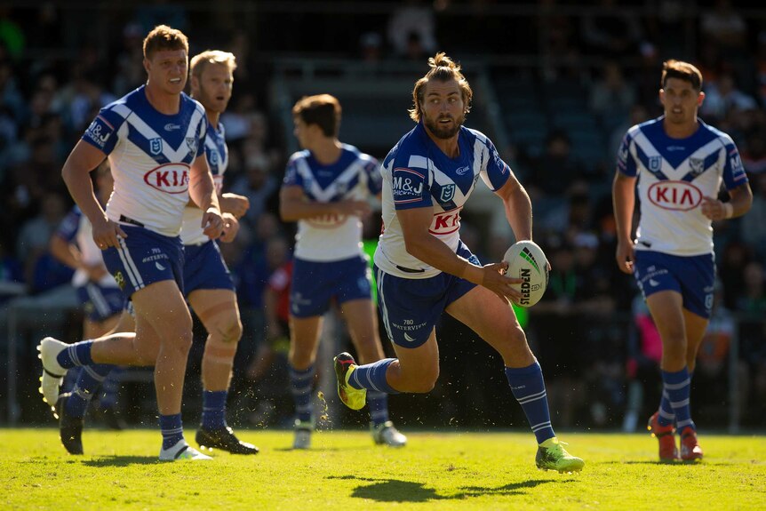 An NRL player runs, shaping to pass the ball to teammates.