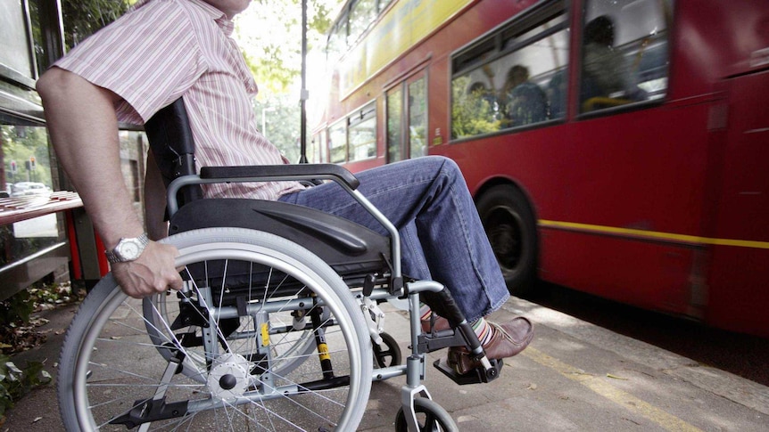 A red bus drives past a person in a wheelchair