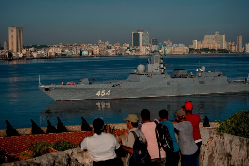 Picture of people looking at a military vessel approaching the shoreline