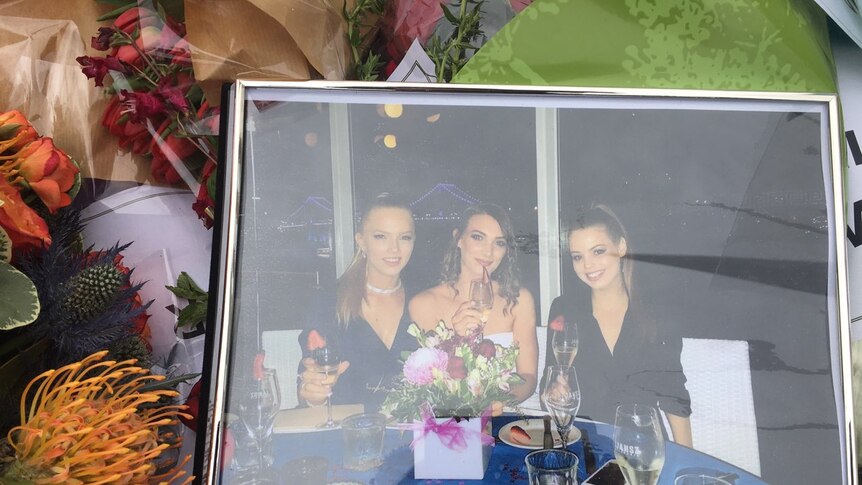 A framed photo of three young women at dinner sits among a bed of flowers