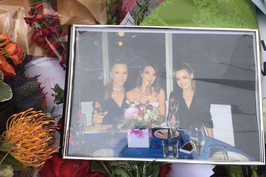 A framed photo of three young women at dinner sits among a bed of flowers