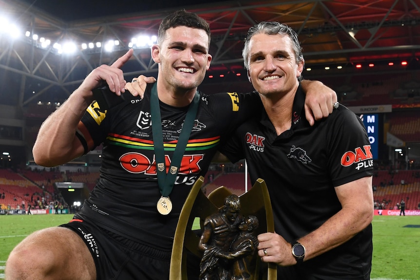 Rugby league player and his coach who is also his dad, poses for a photo with the grand final winner trophy