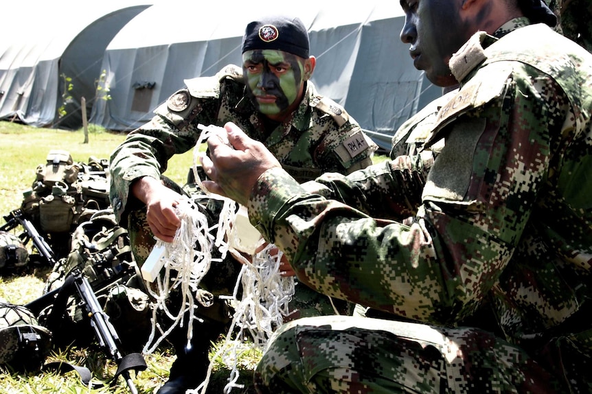 Soldiers in camouflage and army face paint hold a string of Christmas lights.