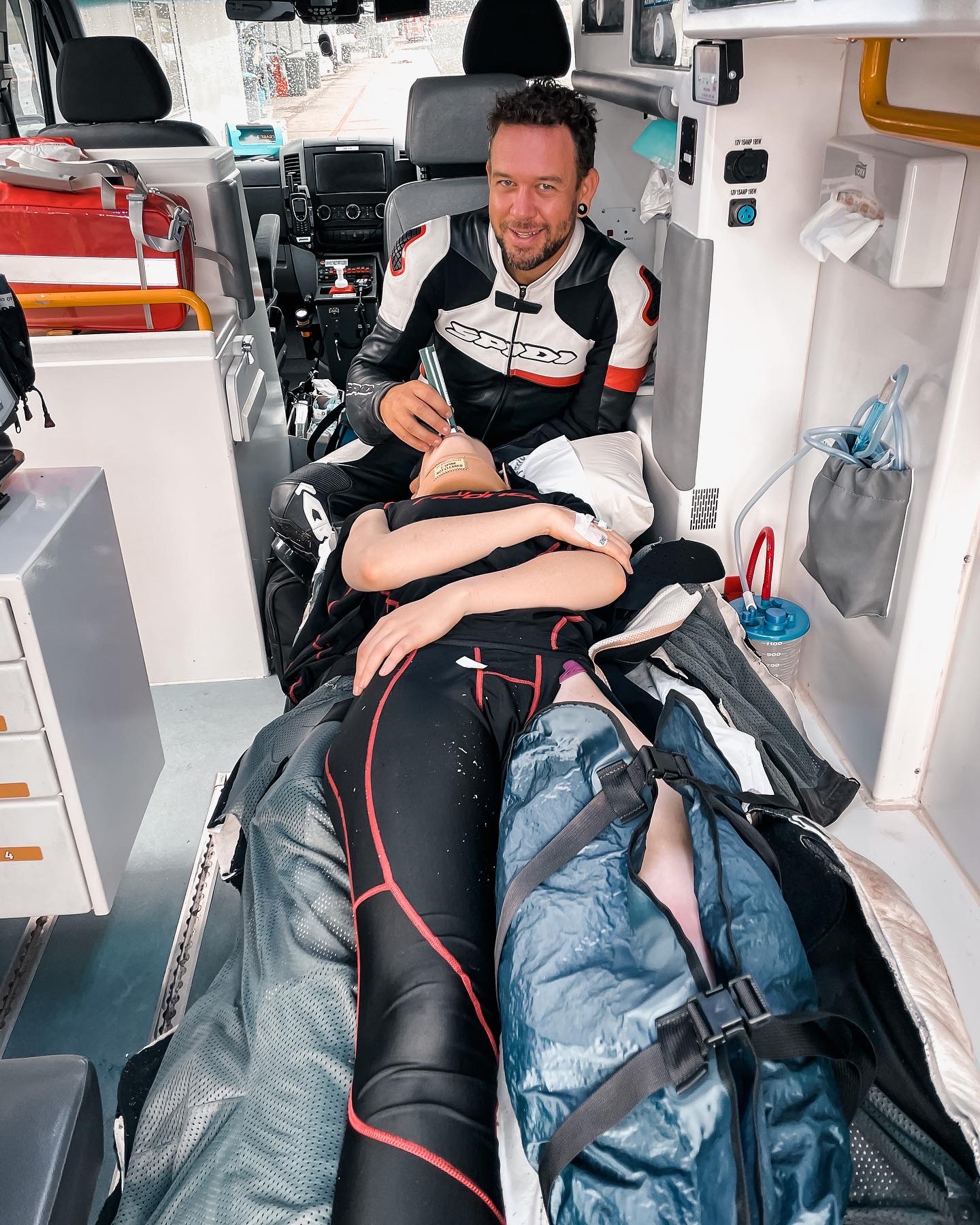 a man holds a green whistle up to the mouth of a woman lying in the back of an ambulance with her knee wrapped in plastic