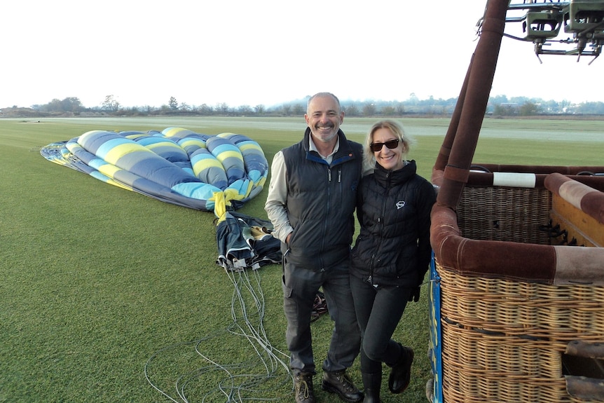 A man and a woman stand smiling beside a deflated hot air balloon.