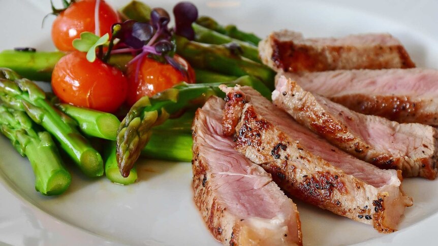 A close up picture of sliced steak with asparagus, tomatoes, and some micro-greens