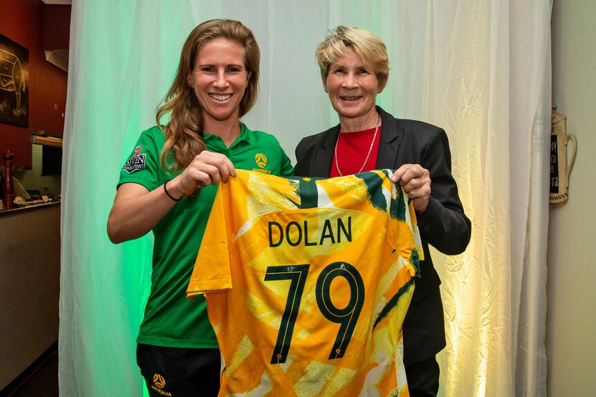 Two Australian female football internationals stand together holding a jersey.