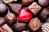 An up-close photo of a box of chocolates with a red heart in the centre.
