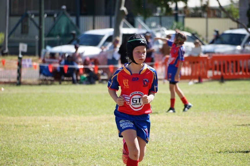 A girl in a rugby union uniform runs on a football field.