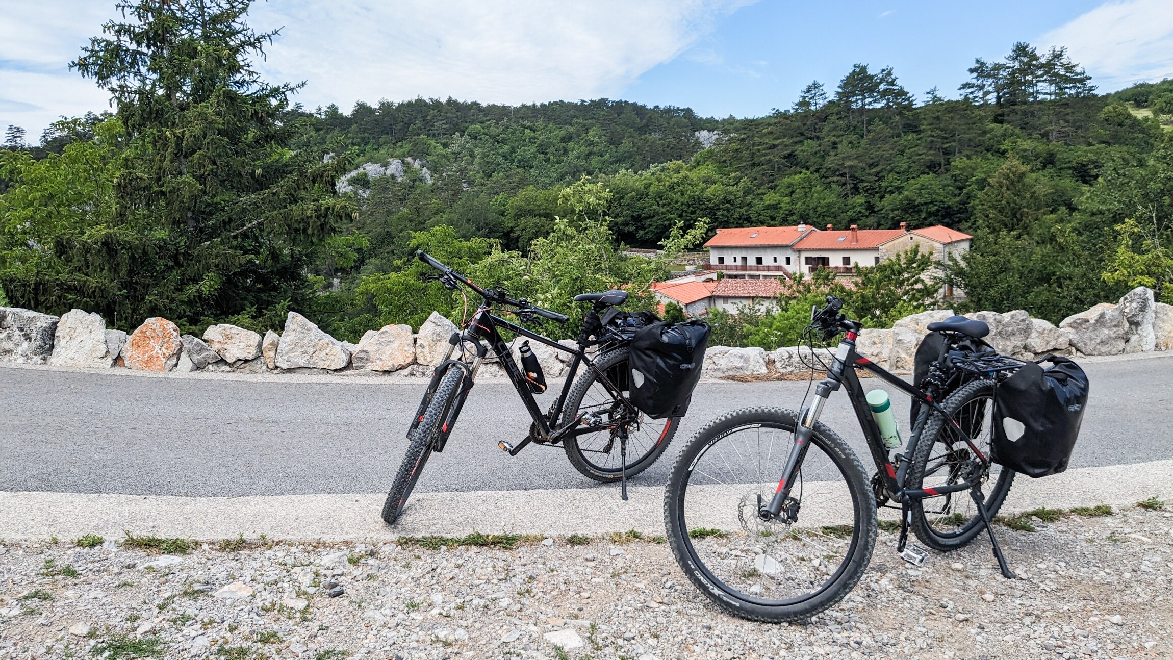 Two black bikes stand propped up on the side of the road in the countryside.