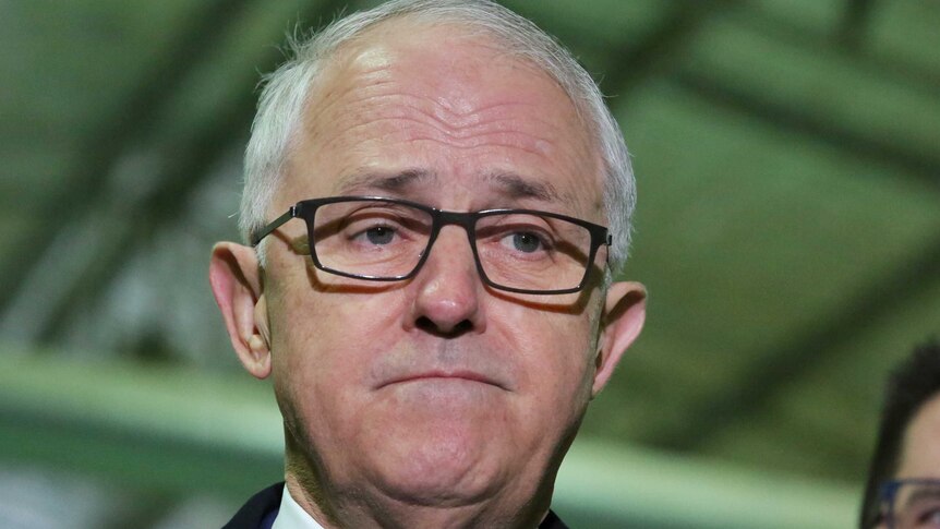 A close-up of Malcolm Turnbull's face shows him frowning. He is wearing dark rimmed glasses