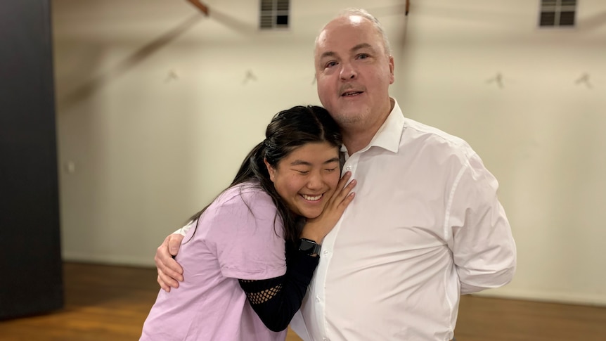 Actors Shelby Brodie and Peter Uniacke hug on stage.