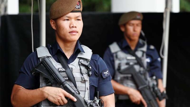 Two Gurkhas stand holding their guns, wearing brown caps