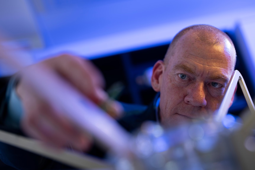 A close-up shot of man's face as he inspects some equipment on a table.