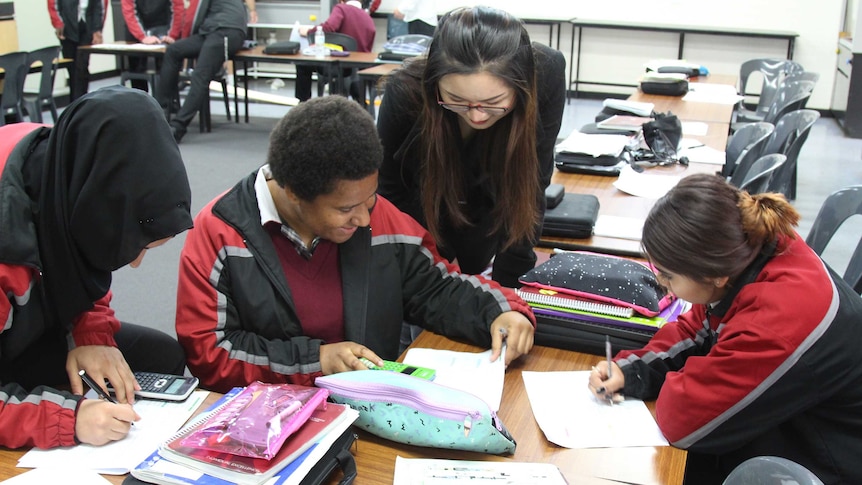 In a classroom, Nabaa Al Gburi, Rowenna Kalimba and Keharn Hudson use calculators and write on a worksheet as Lori Lu looks on.