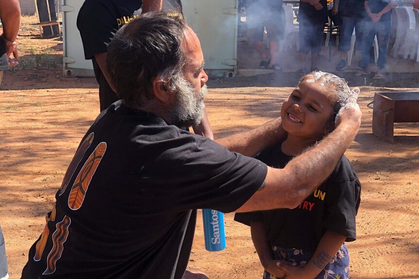 A man paints on a young girls face in preparation for a smoking ceremony.