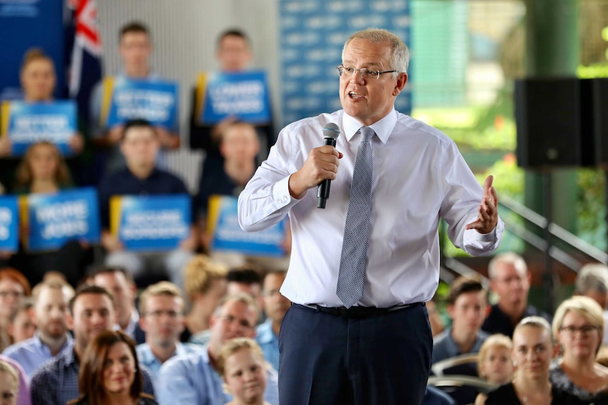 Mr Morrison stands on a stage holding a microphone with supporters surrounding him