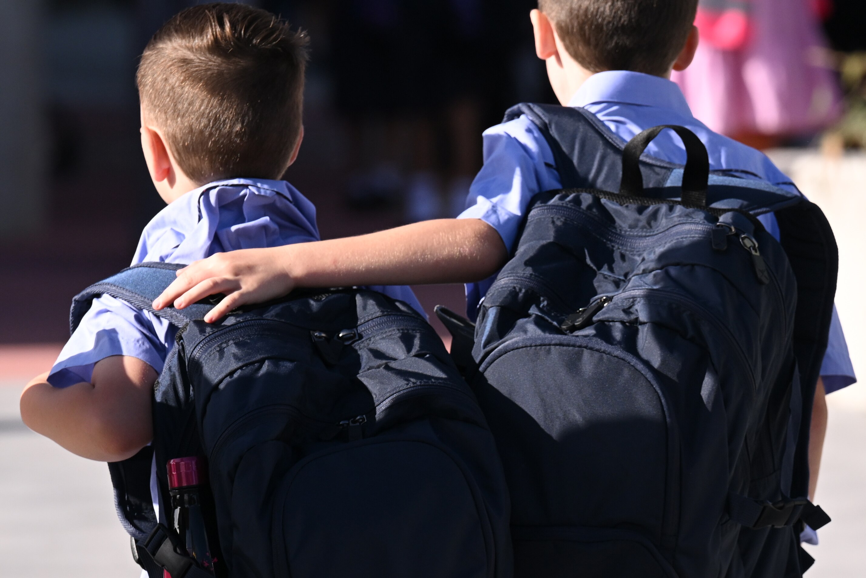 a photo of two young schoolboys, taken from the back, one has his arm around the other's shoulders