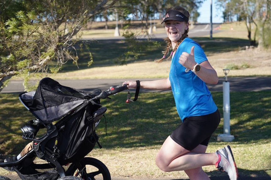 A woman runs while pushing a stroller and gives a thumbs up.