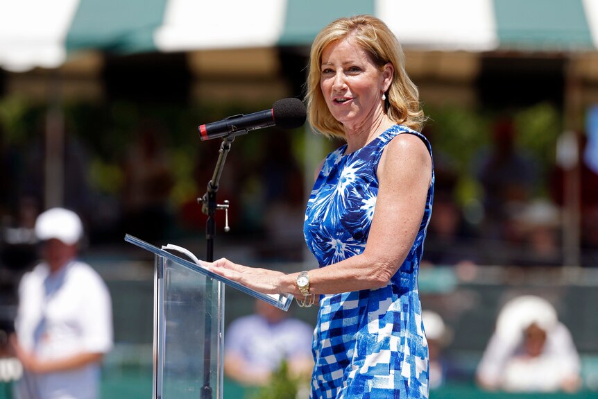 Chris Evert speaks into a microphone, wearing a sleevless dress and a watch on her wrist
