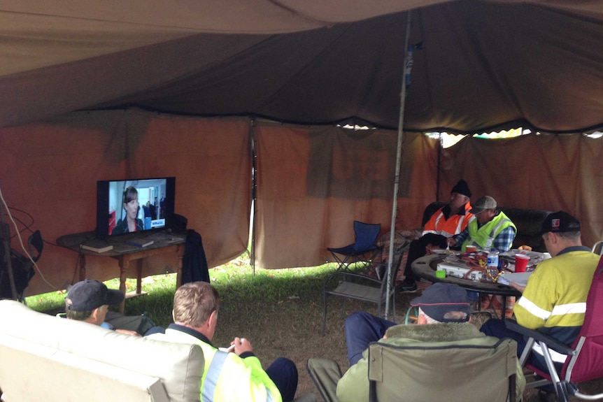 Workers sit under a canvas on lounges watching a television and eating meals in a make-shift camp at Myrtleford.