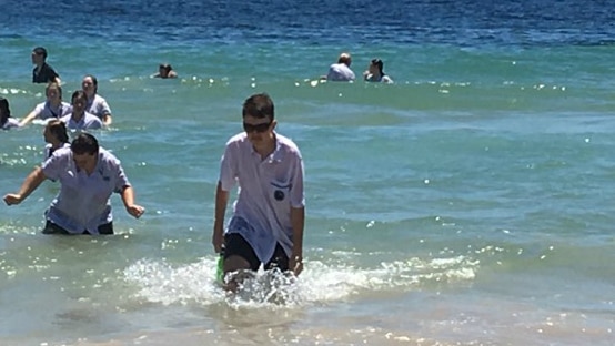 Teenagers in the surf wearing school uniform as part of graduation tradition.