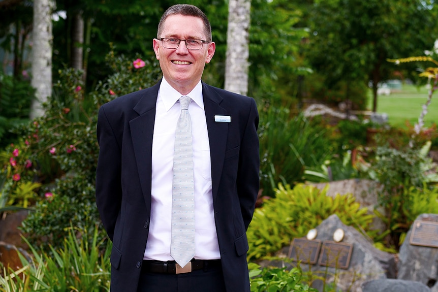Man in suit standing smiling in front of a garden