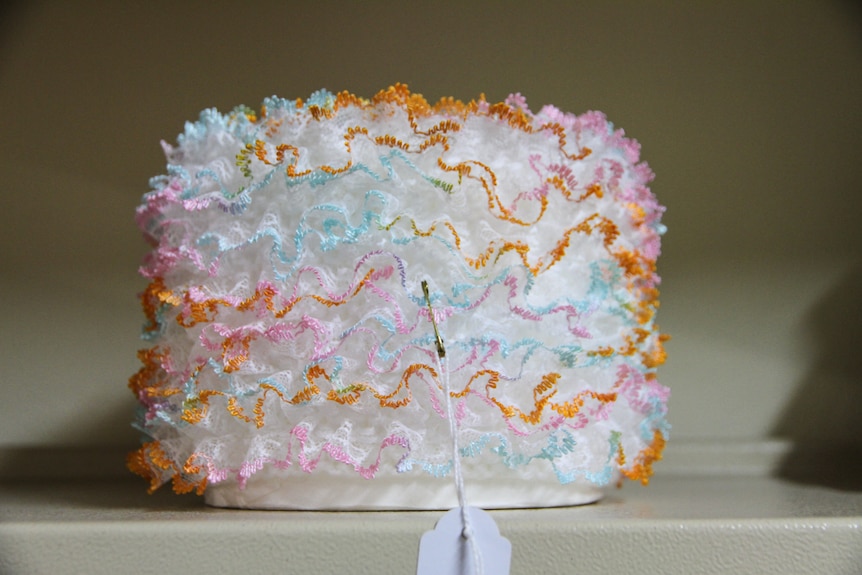 A pretty, fluffy toilet roll holder sits on a shelf. 