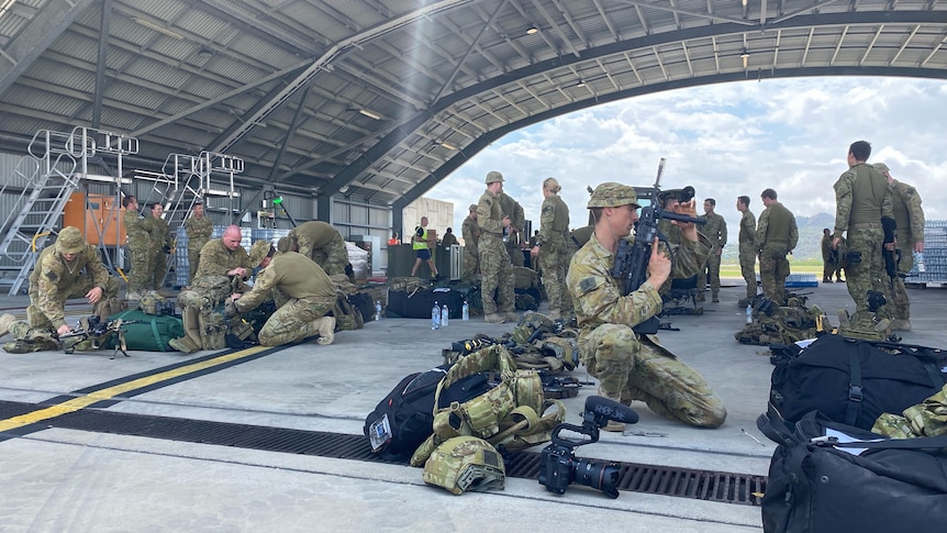 Soldiers kneel and check guns and gear.