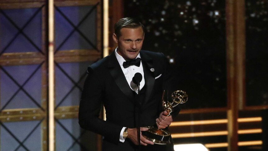 Alexander Skarsgard speaks into the microphone as he holds his trophy