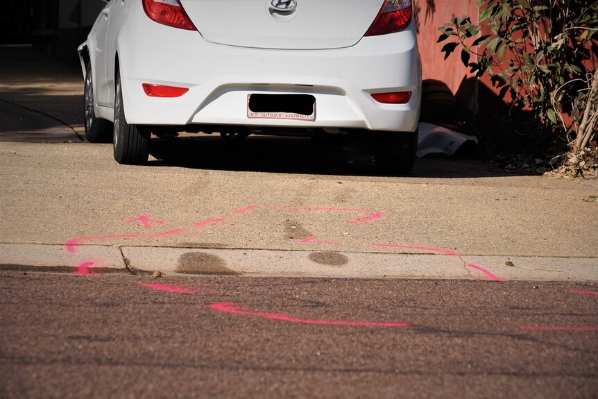 Crashed white car in a driveway in Rapid Creek NT. Sunny day. Trees. Red wall. Pink outline on ground