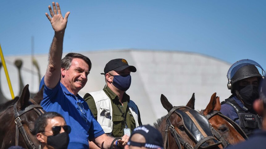 Brazil's President Jair Bolsonaro rides a horse and waves, wearing a blue shirt