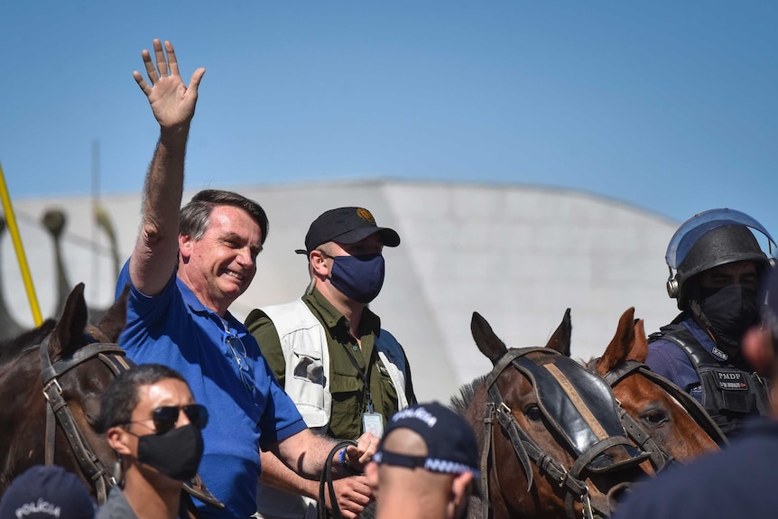 Brazil's President Jair Bolsonaro rides a horse and waves, wearing a blue shirt