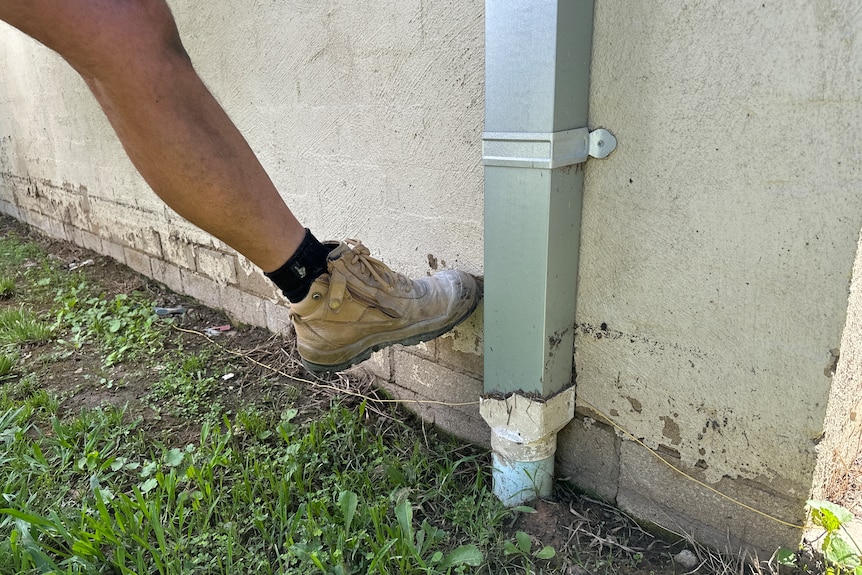 A man uses his boot to point at where the water came up to against the outside of his home.