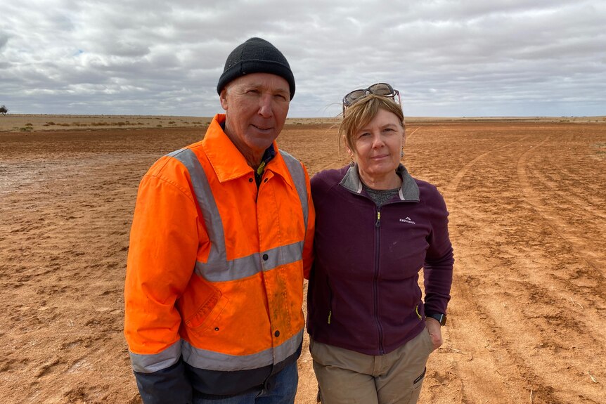 A man and a woman stand together in a farm paddock with no crops. 