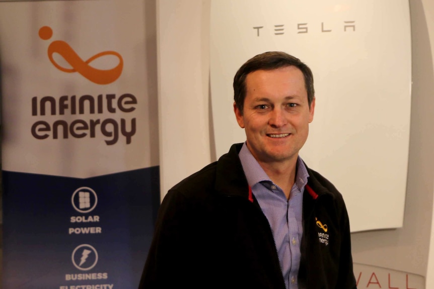 Shane Cremin stands near a tesla power wall battery