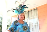 Caren Stevenson stands with large blue hat creation with feathers on her head