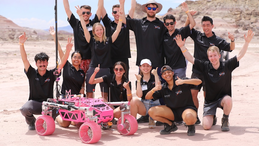 A group of students pose for a celebration photo in Utah desert with their pink rover.