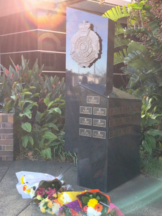 Four bouquets of brightly coloured flowers sit in front of a marble entry a Toowoomba police station.