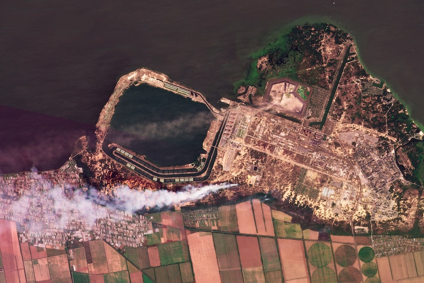 an aerial satellite image of the Zaporizhzhia nuclear power plant showing a plume of smoke rising from a building