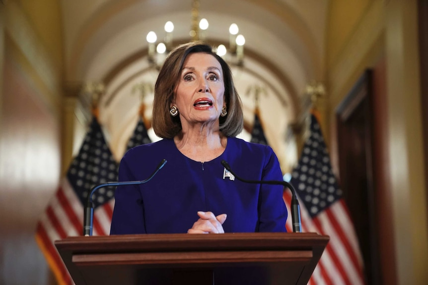 Nancy Pelosi speaks at a podium with two American flags behind her