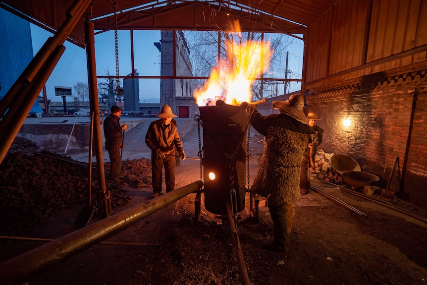 A group of men stoke a pot of molten iron