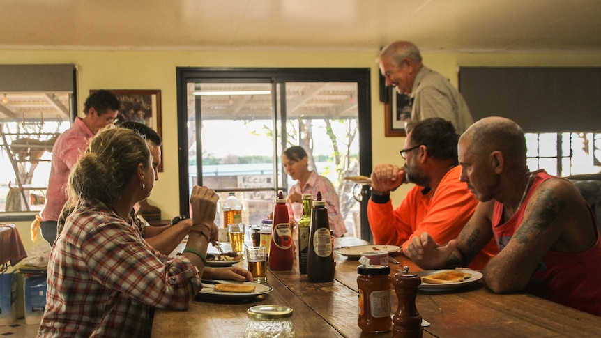 A group of people eat breakfast at a large table in a farmhouse.