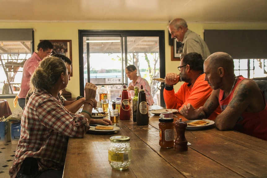 A group of people eat breakfast at a large table in a farmhouse.