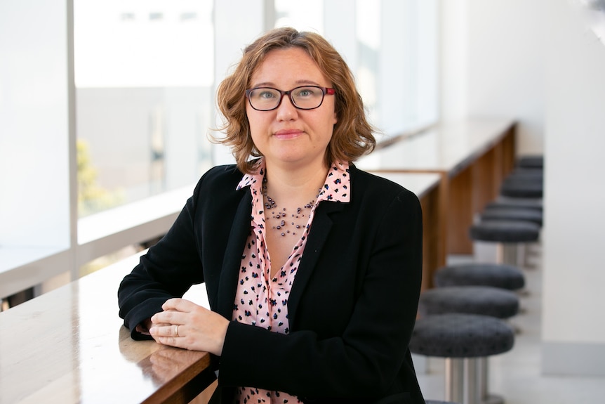 Headshot of Marketing Professor Valentyna Melnyk, sitting at a table wearing glasses, a pink spotted shirt and black jacket
