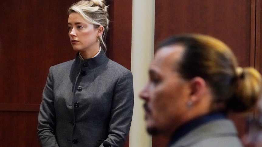 Amber Heard stands in a court room with Johnny Depp in the foreground.