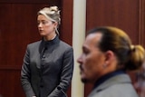Amber Heard stands in a court room with Johnny Depp in the foreground.