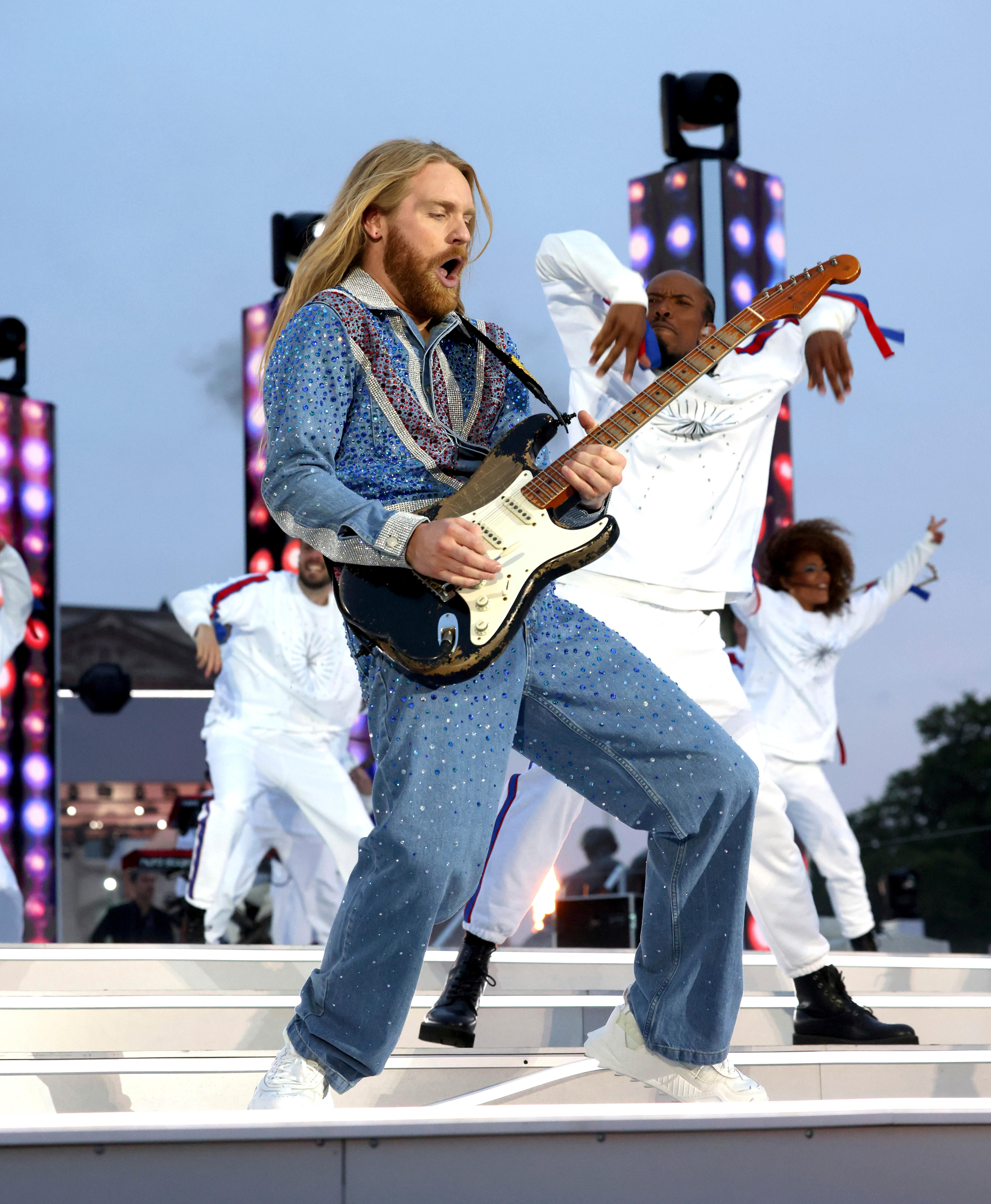 Sam Ryder playing guitar on stage while wearing a sparkly Union Jack bodysuit